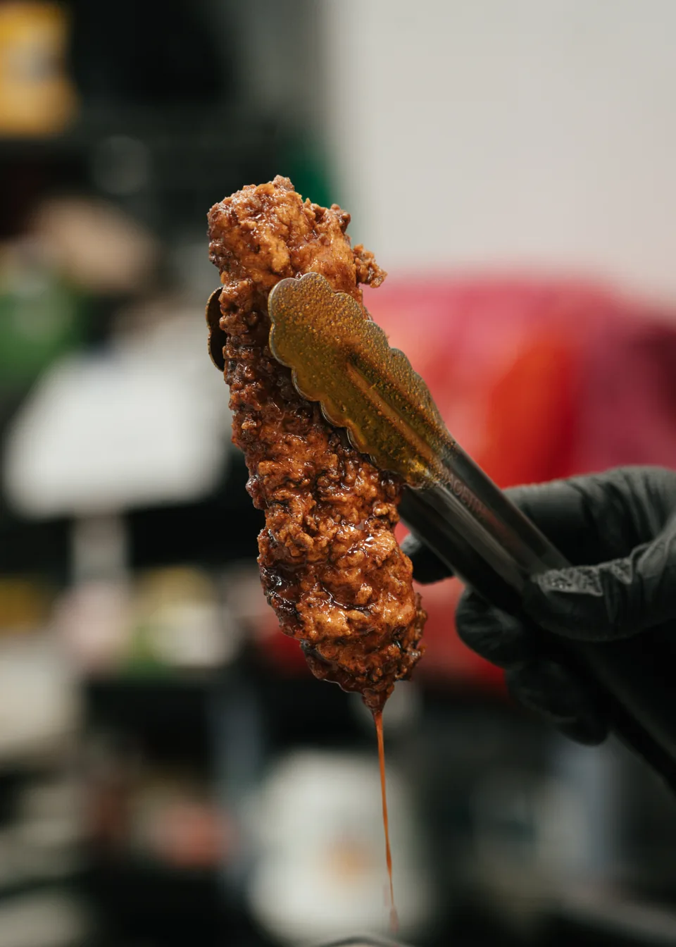 A glazed hot chicken tender lifted with kitchen tongs
