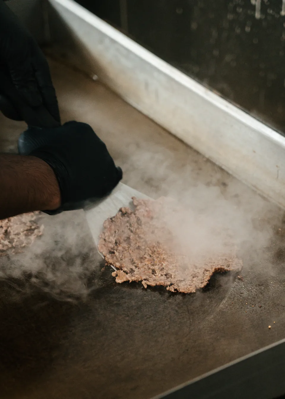 A cook smashing a burger patty on the steaming griddle