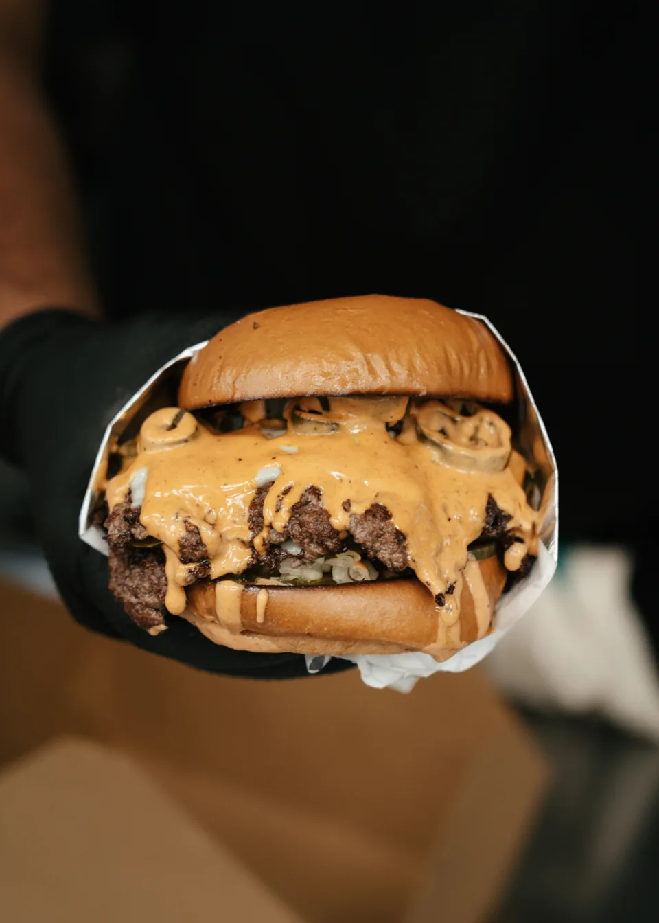A smashed burger with sauce and pickles, held ready to serve